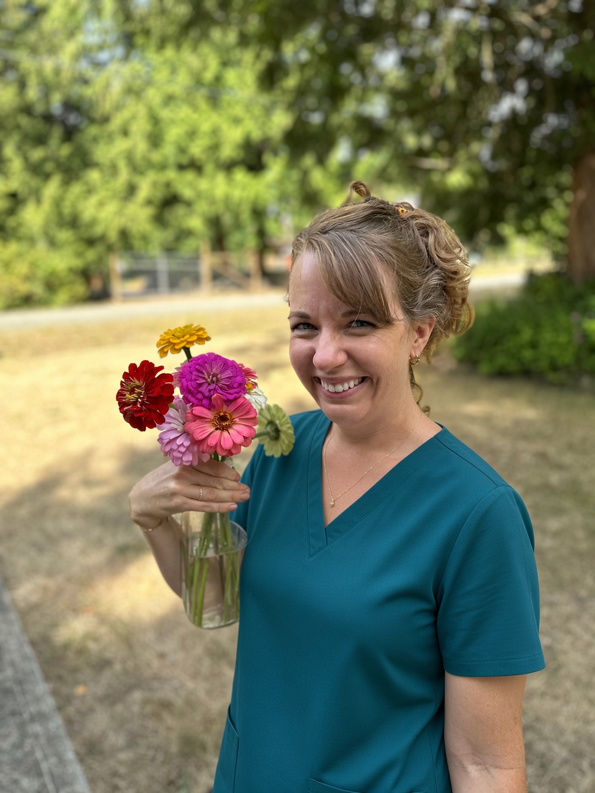 Meghan Campbell, RN, in teal scrubs, holding a small vase of flowers outdoors